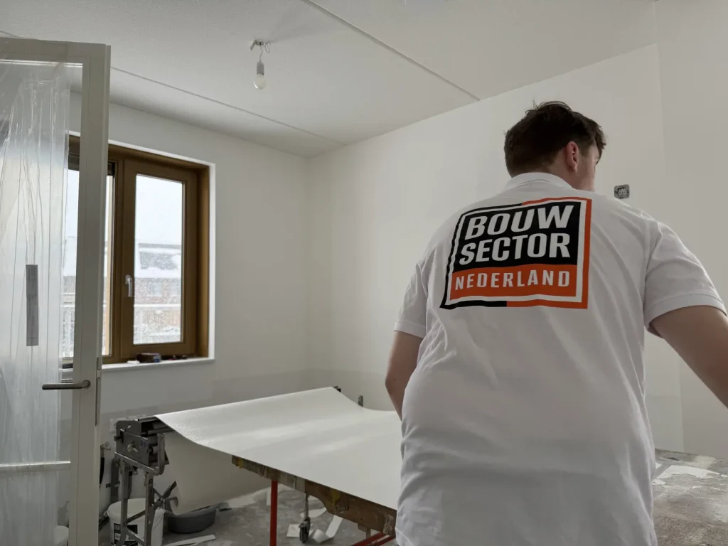 Behanger van Bouwsector Nederland rolt een baan vlies uit over de plaktafel in een lege kamer