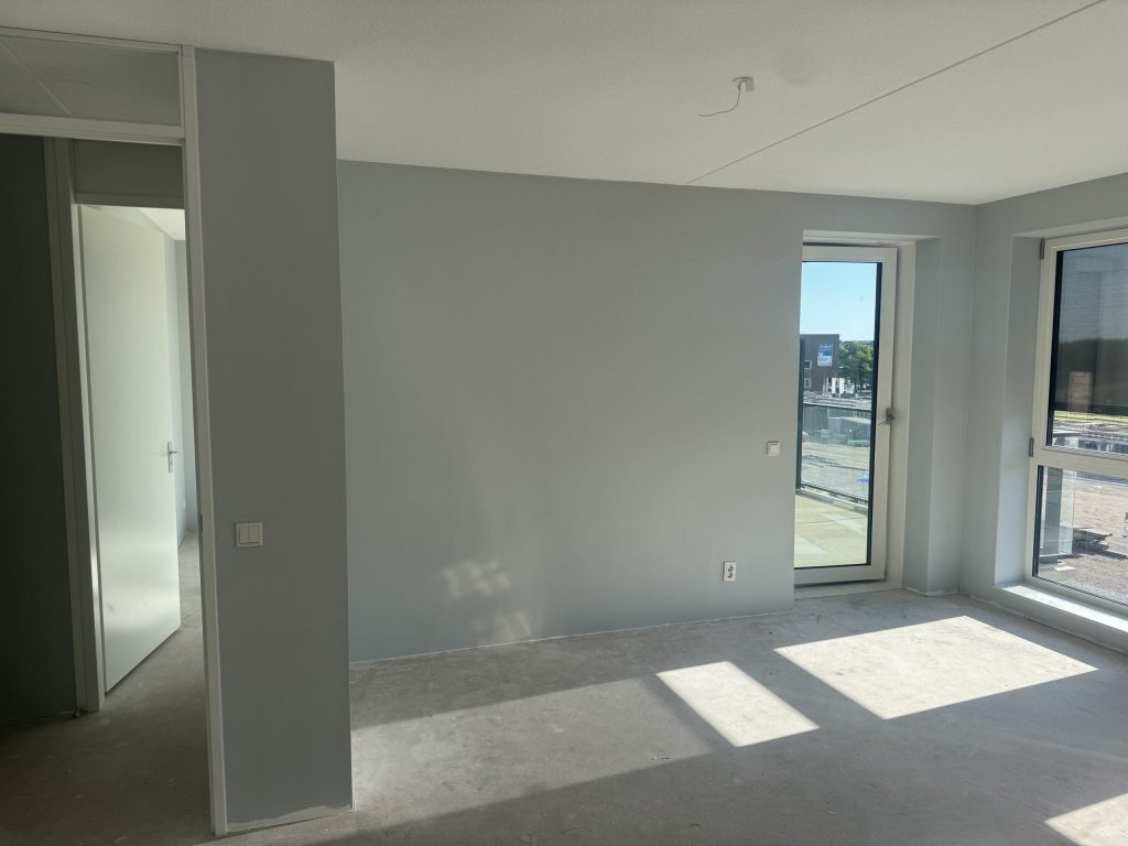 Kamer in een appartement met lichtblauw gesausde wanden en een deur naar het balkon