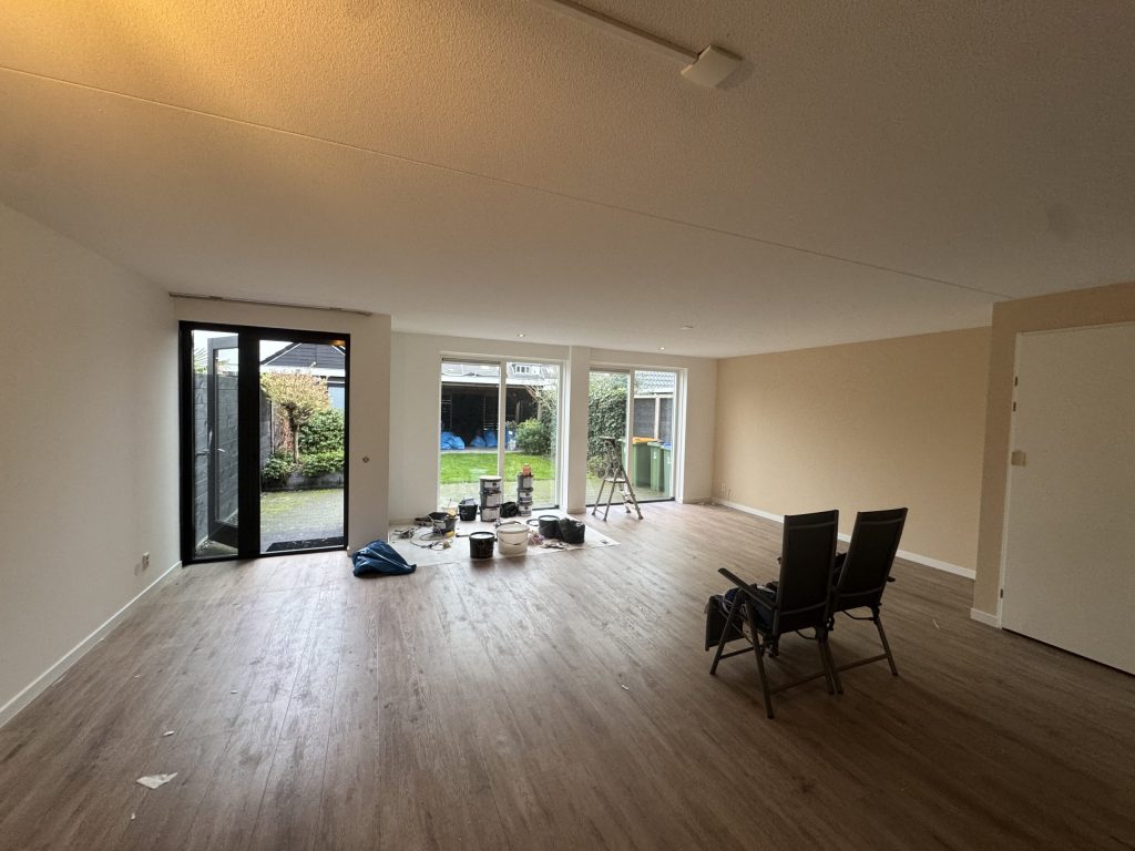Ruime woonkamer van een bestaand huis met lichte wanden, een houten vloer en openslaande tuindeuren