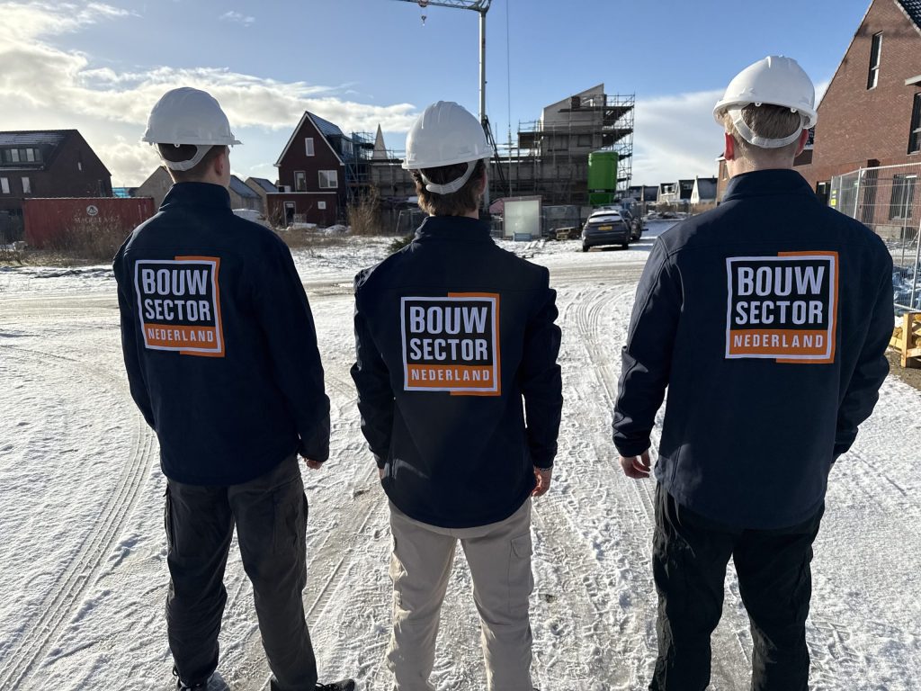 Drie vakmensen van Bouwsector Nederland met witte helm en bedrijfsjas op een nieuwbouwplaats in de sneeuw